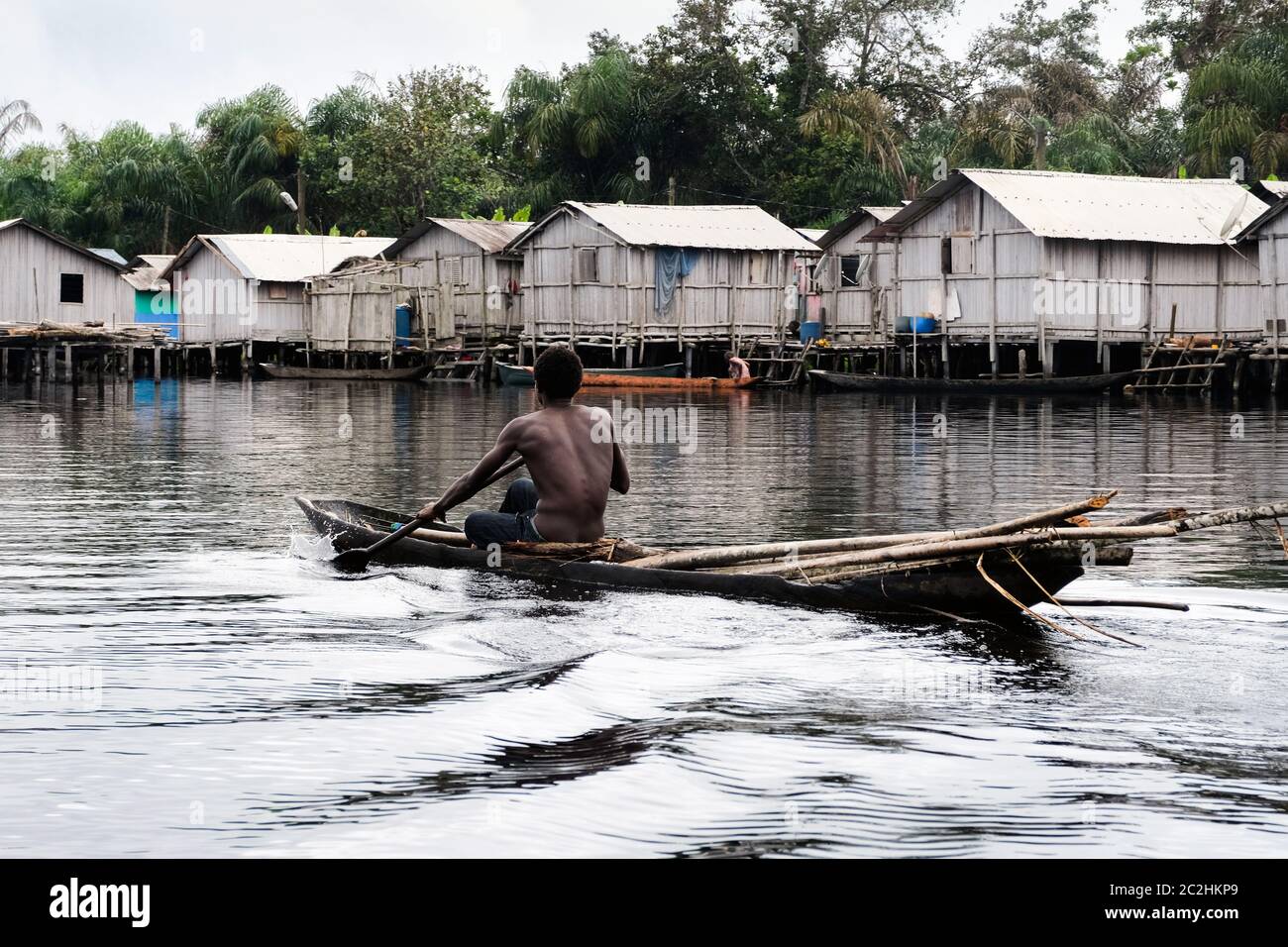 Mann in einem Ausgußboot vor den Hütten des Stelzendorfes Nzulezo im Amansura See, Ghana, Afrika Stockfoto