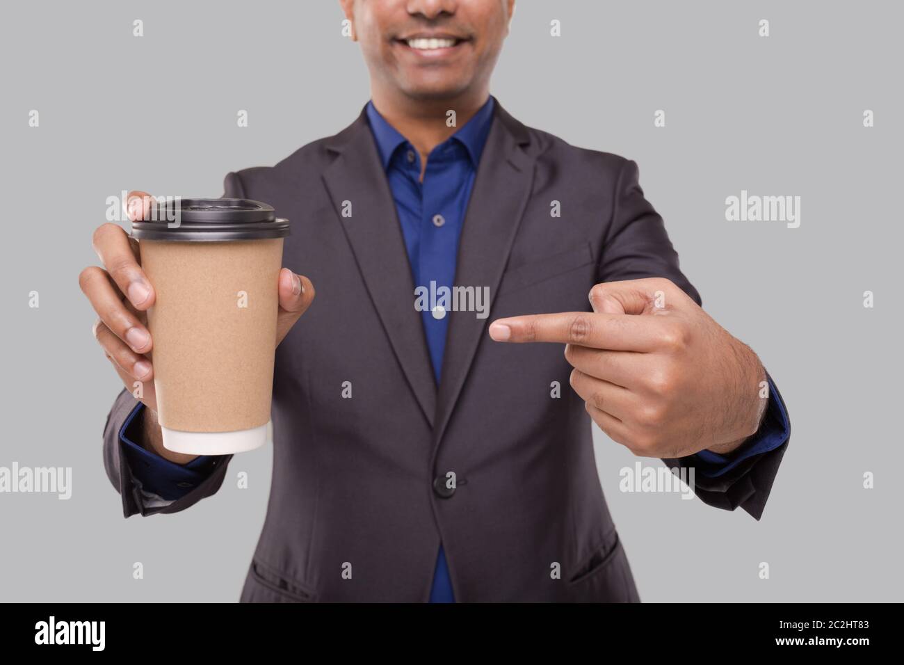 Geschäftsmann zeigt auf Coffee to Go Tasse isoliert Nahaufnahme. Indischer Geschäftsmann mit Kaffee Take Away Tasse in den Händen Stockfoto