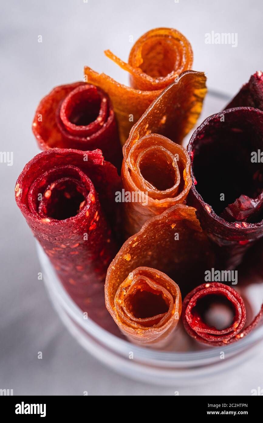 Obstpastilien in Glas Tasse auf Stein Beton Hintergrund. Bio-zuckerfreies Roll-up-Lebensmittel aus Himbeere, Erdbeere, Pfirsich und Apfel. Veganes Zuhause Stockfoto