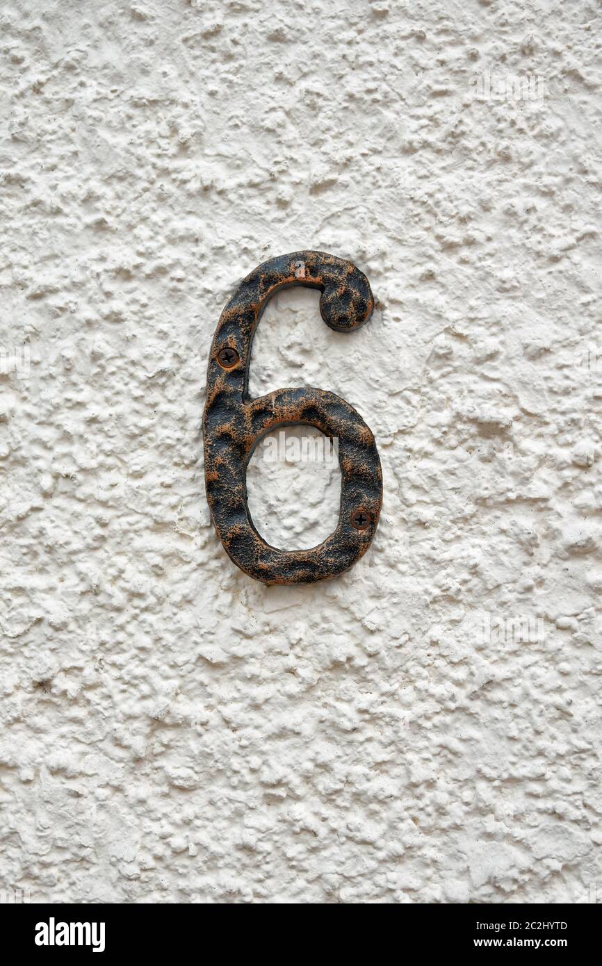 Isolierte Nummer 6 in verwittertem Eisen, das an weißgetünchten harled Wand hängt Stockfoto