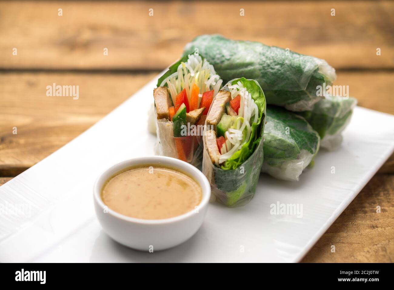 Frische vietnamesische Frühlingsrollen, ideal als gesunde Vorspeise mit Erdnussbutter-Sauce zum Eintauchen. Die Platte ist auf einem Holzhintergrund platziert. Stockfoto