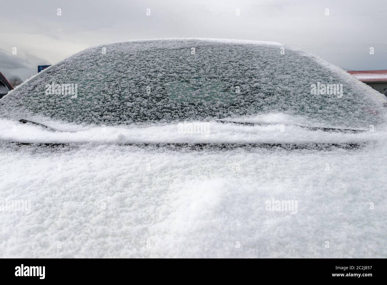 Nahaufnahme eines Autos mit schneebedeckter Windschutzscheibe und Motorhaube. Das Auto ist nicht identifizierbar. Wolkenbedecktem Himmel über. Stockfoto