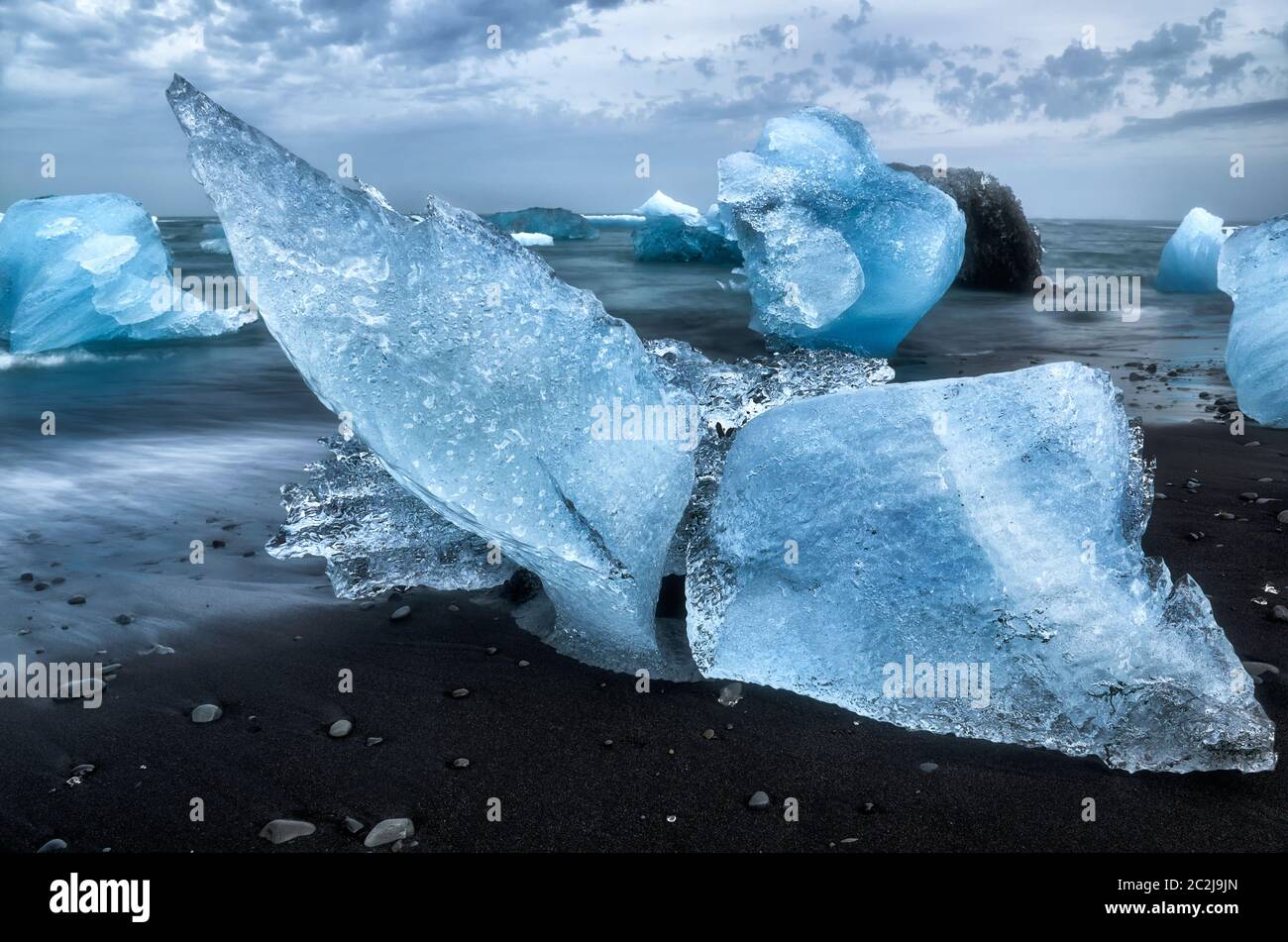 Eisblöcke, die wie ein Walschwanz aussehen, mit schwarzem Sand und glattem Wasser am Diamond Beach Island Stockfoto