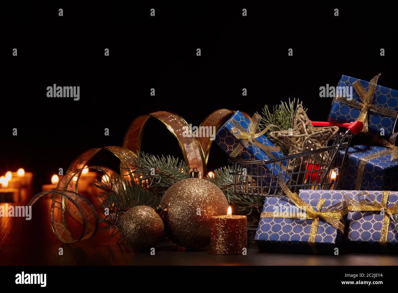 Einkaufswagen, Geschenkboxen und Weihnachtsdekoration mit brennenden Kerzen und Tannenzweig auf schwarzem Hintergrund, Weihnachten und Neujahr einkaufen. Stockfoto