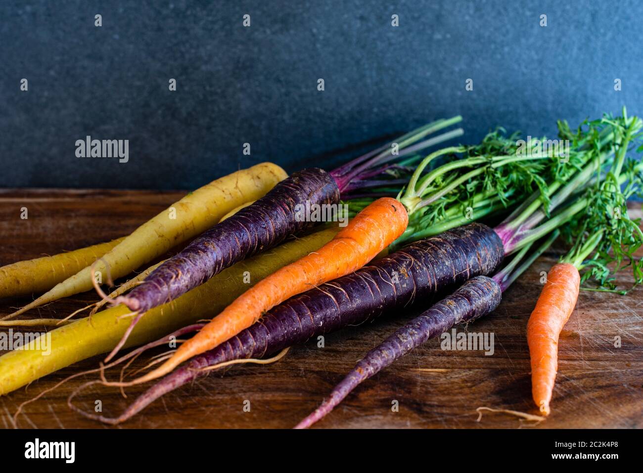 Bunte Erbstück Karotten einschließlich lila, orange und gelb auf einem Holzbrett mit dunklem Hintergrund und Kopierraum Stockfoto