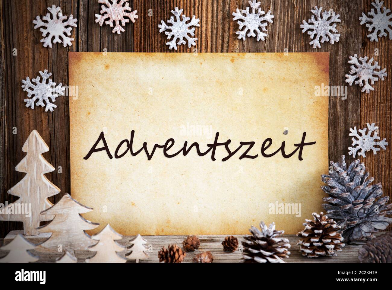 Altes Papier mit deutschem Text bedeutet Adventszeit Adventszeit. Weihnachtsdekoration wie Baum, Tannenzapfen und Schneeflocken. Braun Holz- Hintergrund Stockfoto