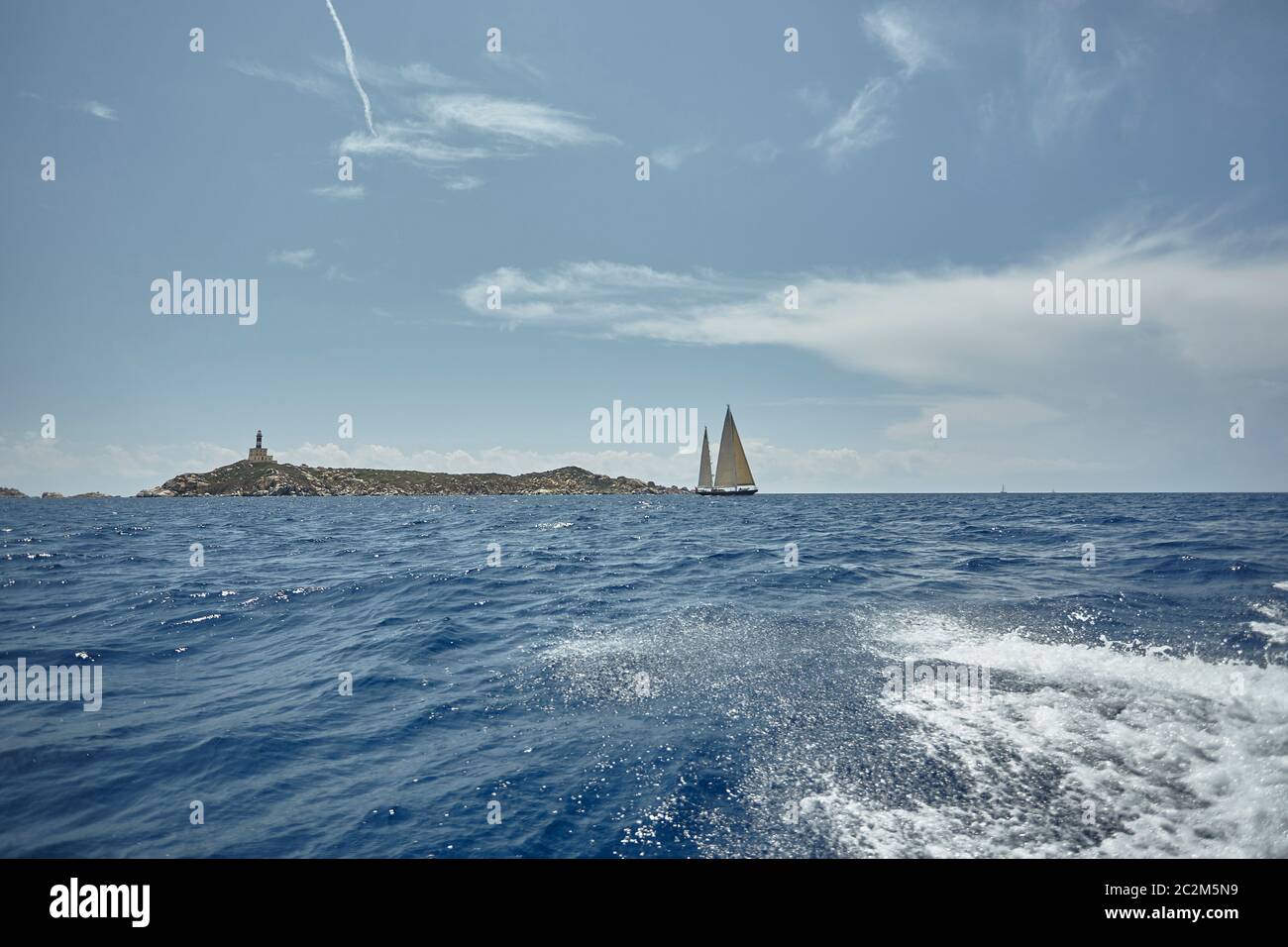 Zwei Segelboote Segeln im Meer vor einer herrlichen Landschaft: ein Leuchtturm am Ende einer Klippe trifft zwischen Himmel und Meer. Stockfoto