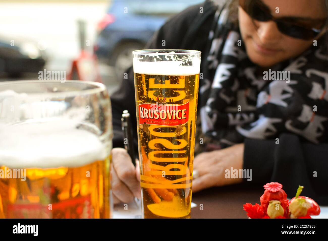 Eine Frau, die dunkle Gläser trägt und ein Bier trinkt, füllt Postkarten in einem Straßencafé in Budapest aus. Stockfoto