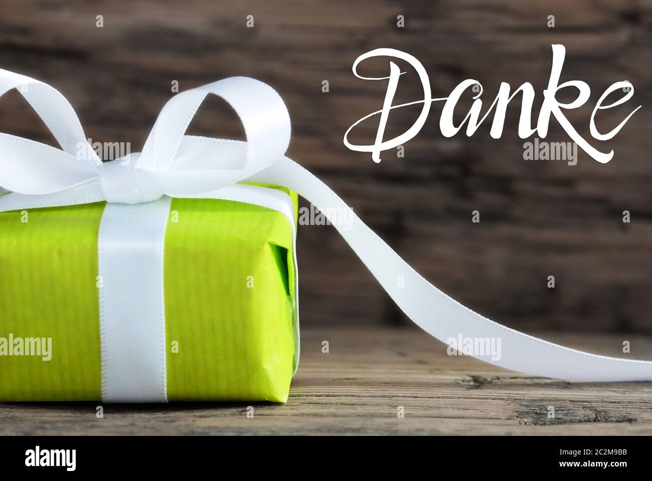 Etikett mit Deutschen Kalligraphie Danke, Danke. Eine grüne Geschenk mit weißen Bogen. Braun Holz- Hintergrund Stockfoto