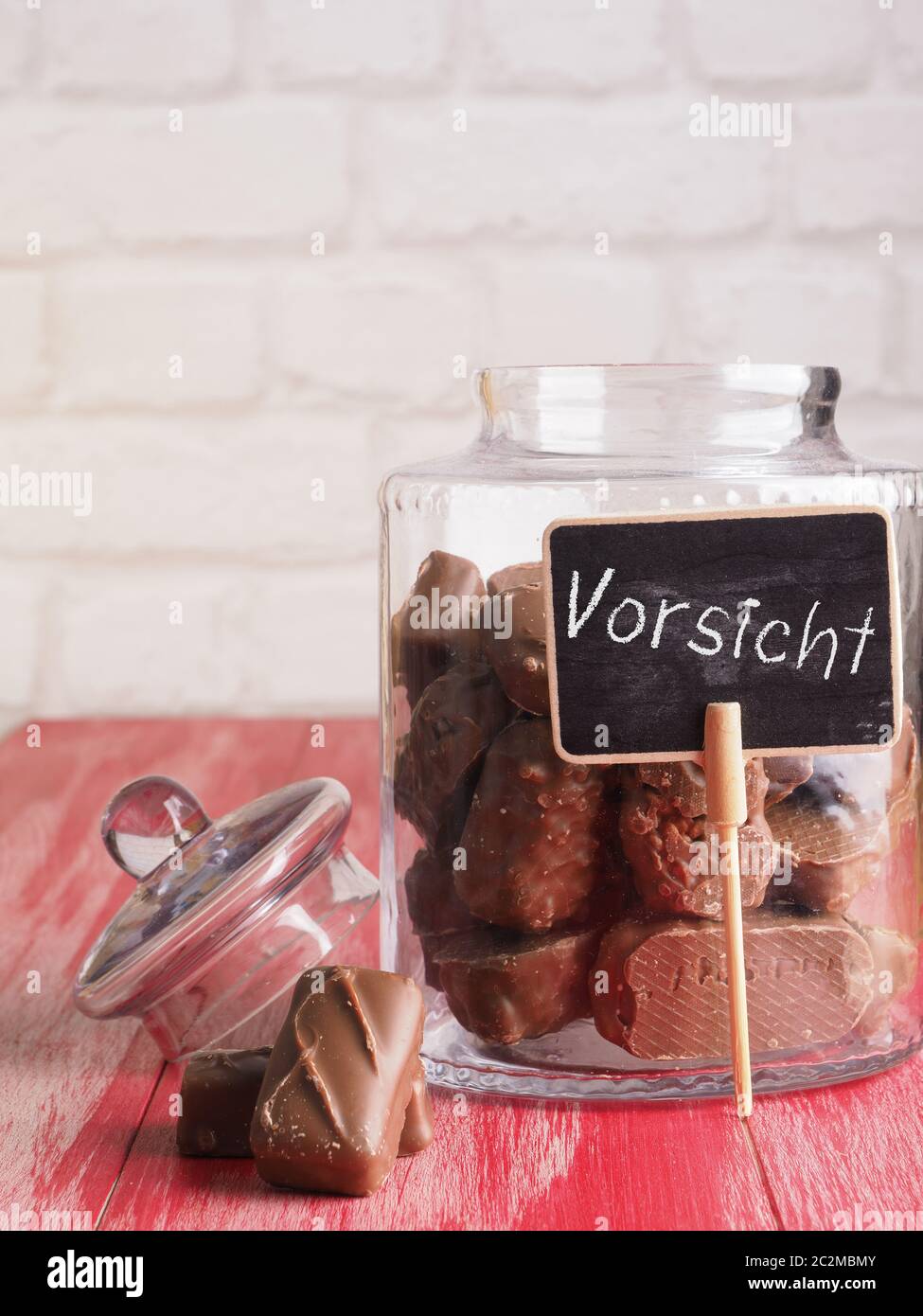 Glas mit Schokolade auf einem hölzernen Küchentisch, kleine Schiefertafel mit der HGerman Wort der Achtung oder Vorsicht! Ungesunde Konzept Essen Stockfoto