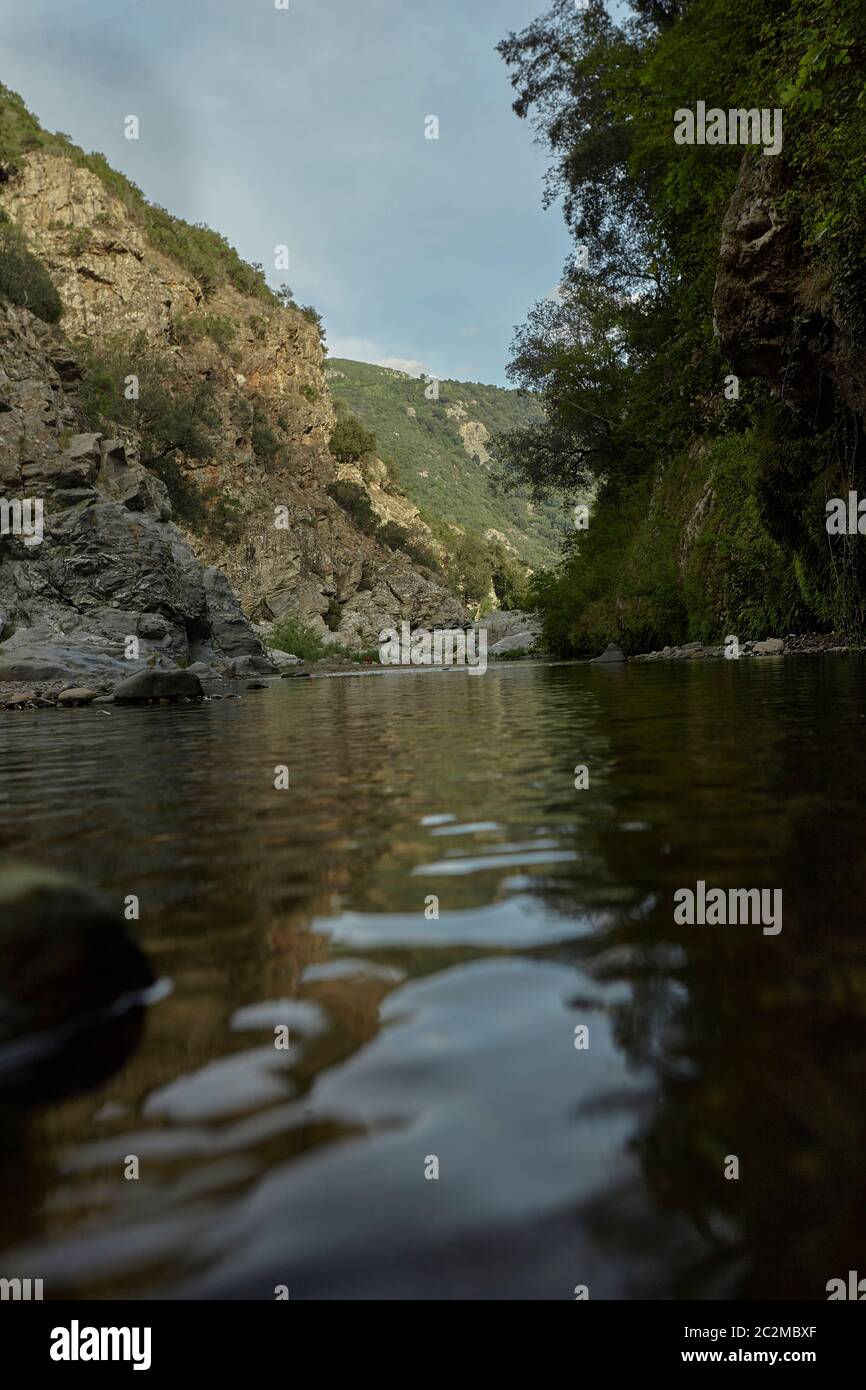 Felswand mit Vegetation bedeckt ist, die Grenze der Wasserlauf in den Bergen mit verschiedenen Felsen, die aus dem Wasser steigen: Die Ansicht von Sa Stid Stockfoto