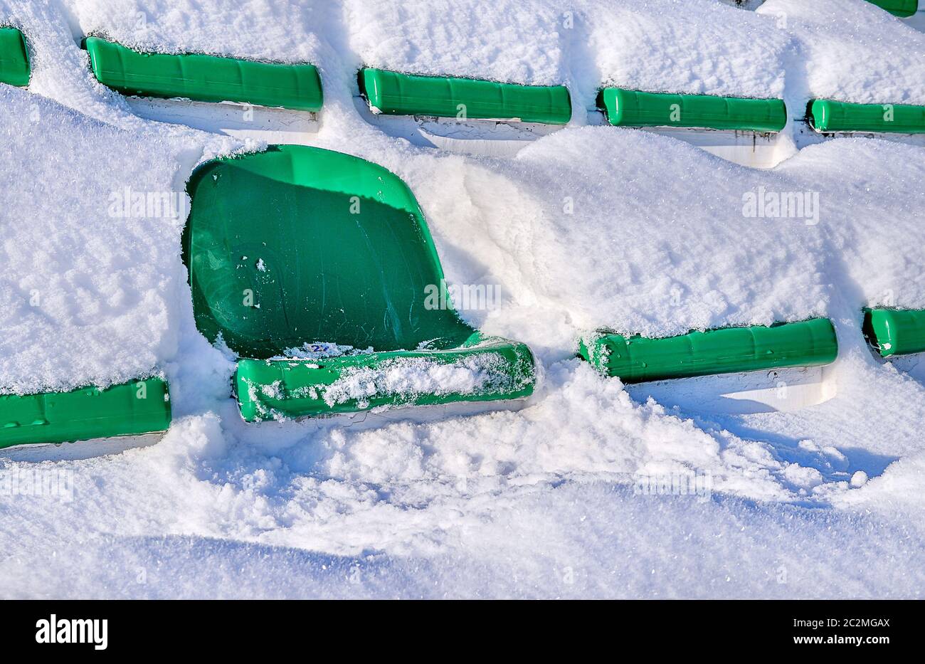 Grüne Sitze eines Sportstadions, mit Schnee bedeckt. Das Konzept der Schließung der Sommersaison der Spiele. Stockfoto
