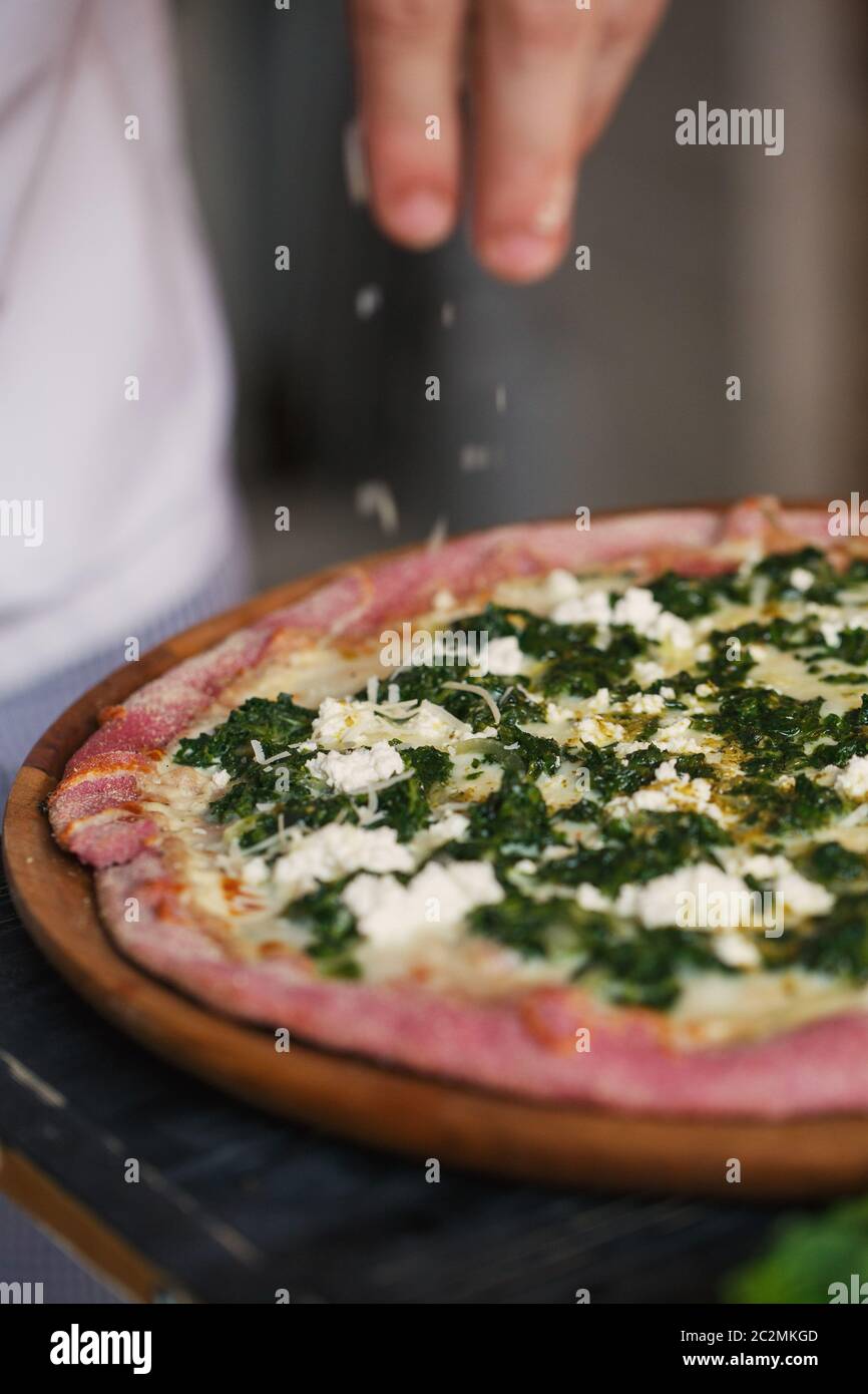 Die hend von Cook ist das Verzieren Pizza mit Käse und Kräutern. Clouse. Stockfoto