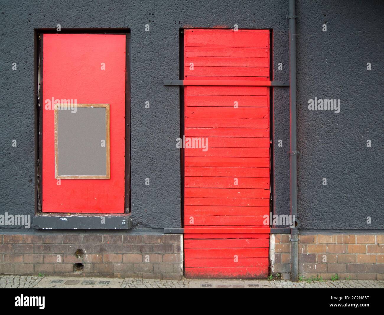 Frontansicht einer grau verputzten Außenwand mit rot verschlossenem Tür- und Fenster auf dem Stadtweg in Berlin 2019. Stockfoto