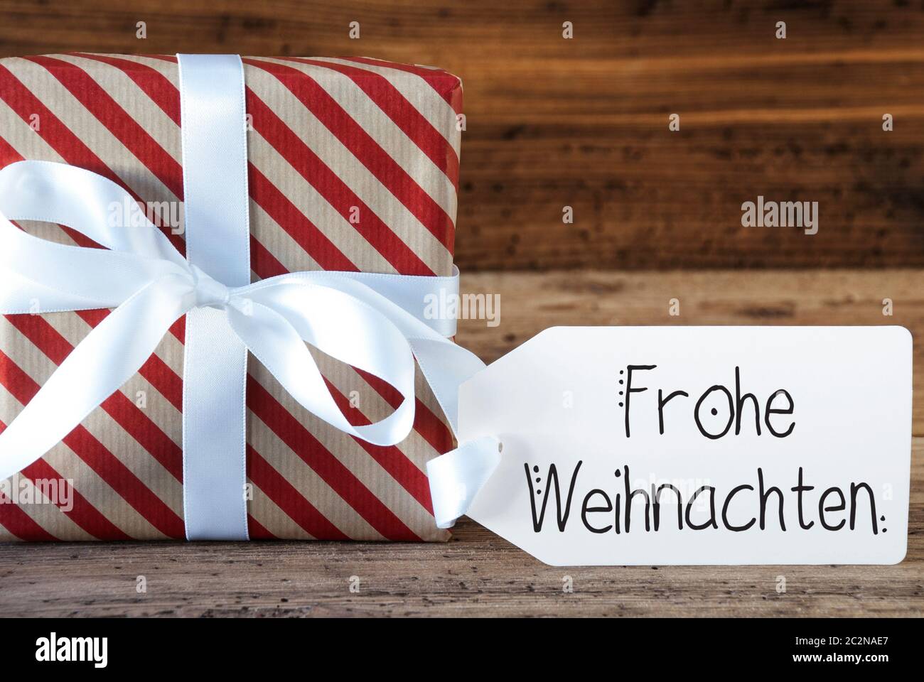 Ein Weihnachtsgeschenk mit Label mit Deutschen Kalligraphie Frohe Weihnachten bedeutet, frohe Weihnachten. Geschenkpapier mit Schleife Stockfoto