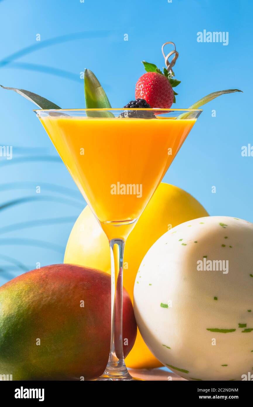 Nahaufnahme eines appetitlichen martiniglases mit Orangensaft mit Blättern und einem Spieß mit Brombeere und Erdbeere, mit einer Mango, einer Honigkugelmelone Stockfoto