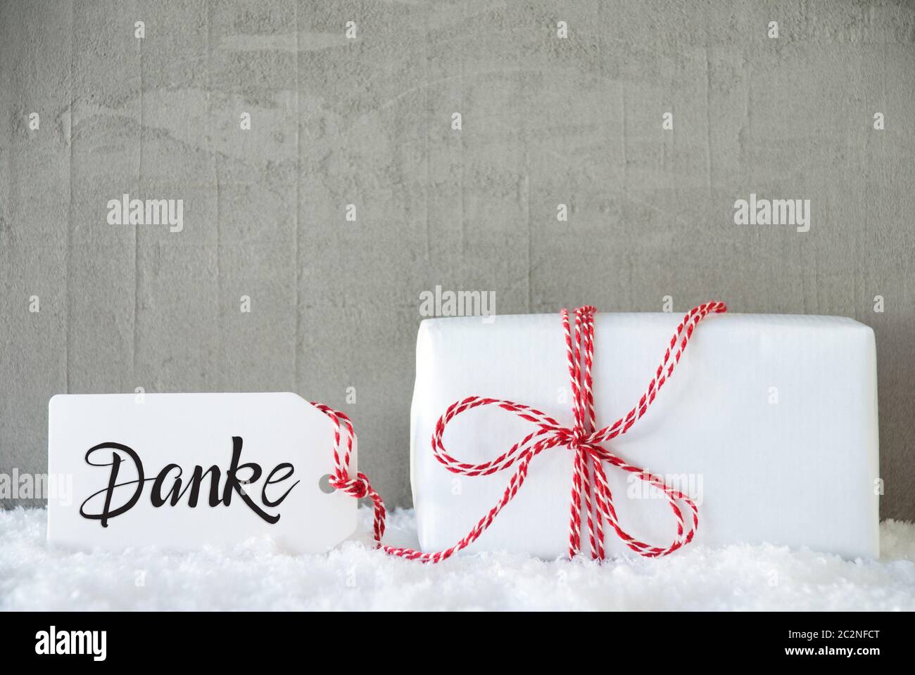 Etikett mit Deutschen Kalligraphie Danke, Danke. Eine weiße Geschenk mit roter Schleife. Grauer Beton Hintergrund mit Schnee Stockfoto