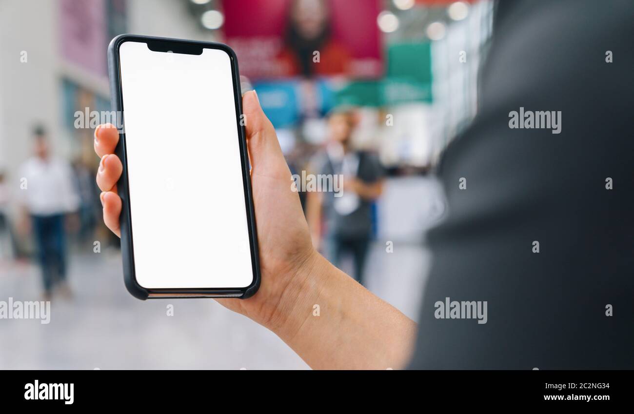 Weibliche Hand mit schwarzem Handy mit weißem Bildschirm auf einer Messe, Copyspace für Ihren individuellen Text. Stockfoto