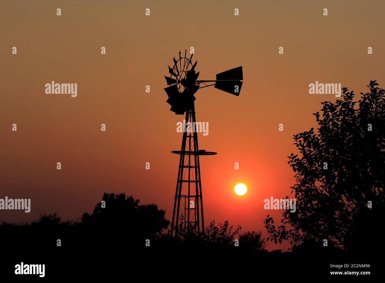 Kansas Windmill Silhouette mit einem hellen Orange Sunset und Baum Silhouetten. Stockfoto