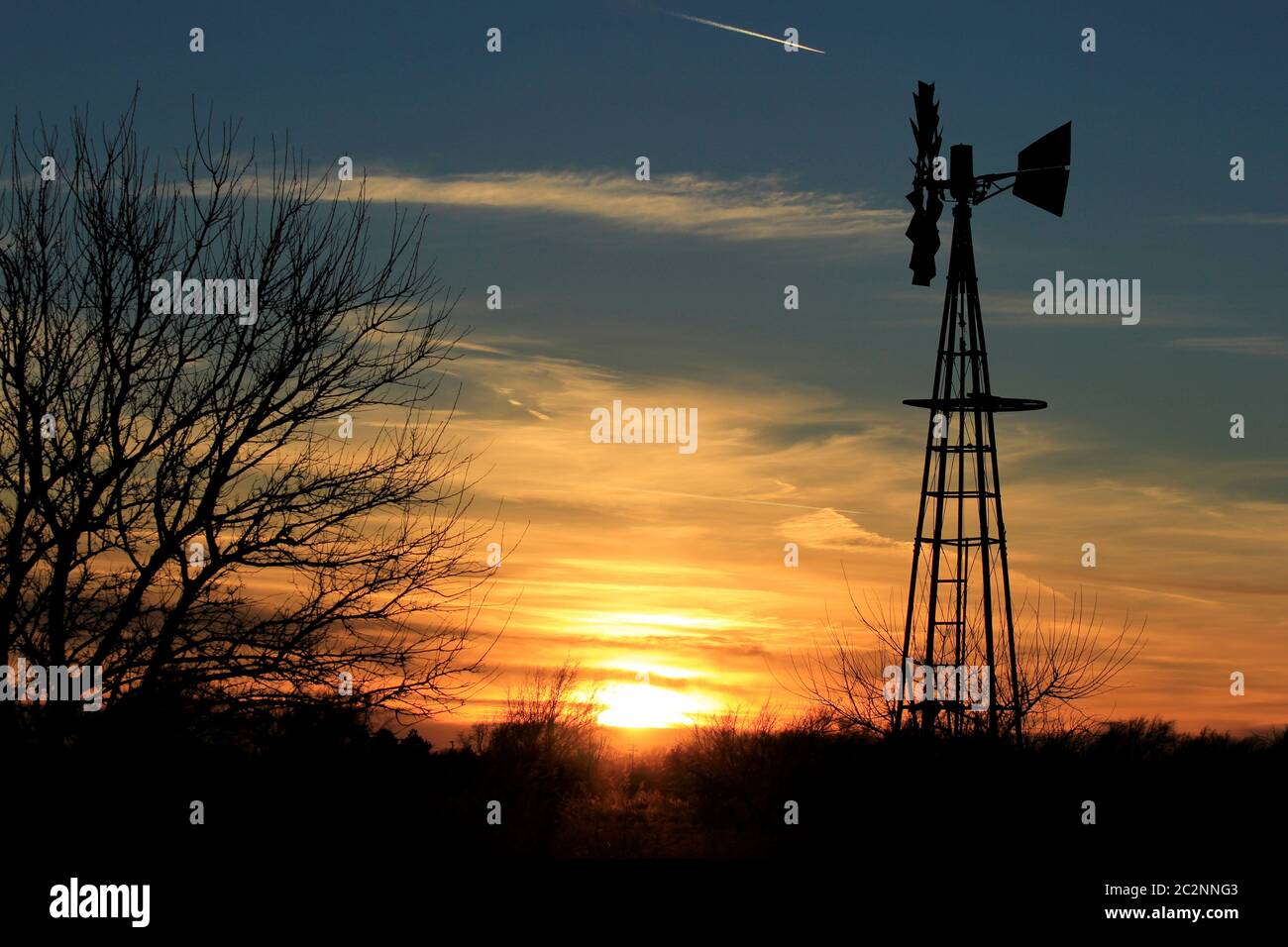 Kansas Windmill Silhouette mit einem hellen Orange Sunset und Baum Silhouetten. Stockfoto