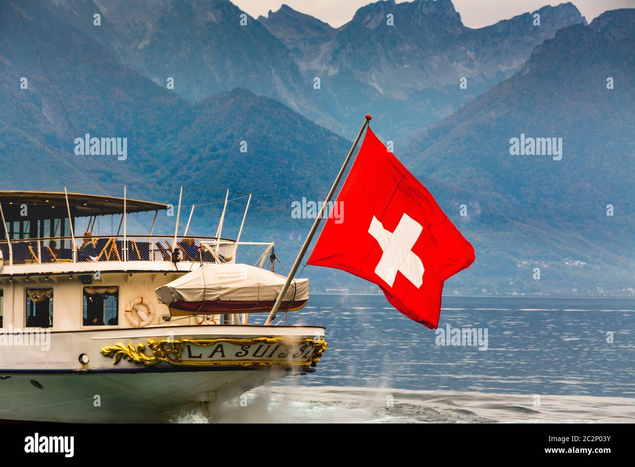 Der majestätische Raddampfer (La Suisse) gleitet über den Genfer See mit der Schweizer Flagge, die vor der atemberaubenden Bergkulisse winkt Stockfoto