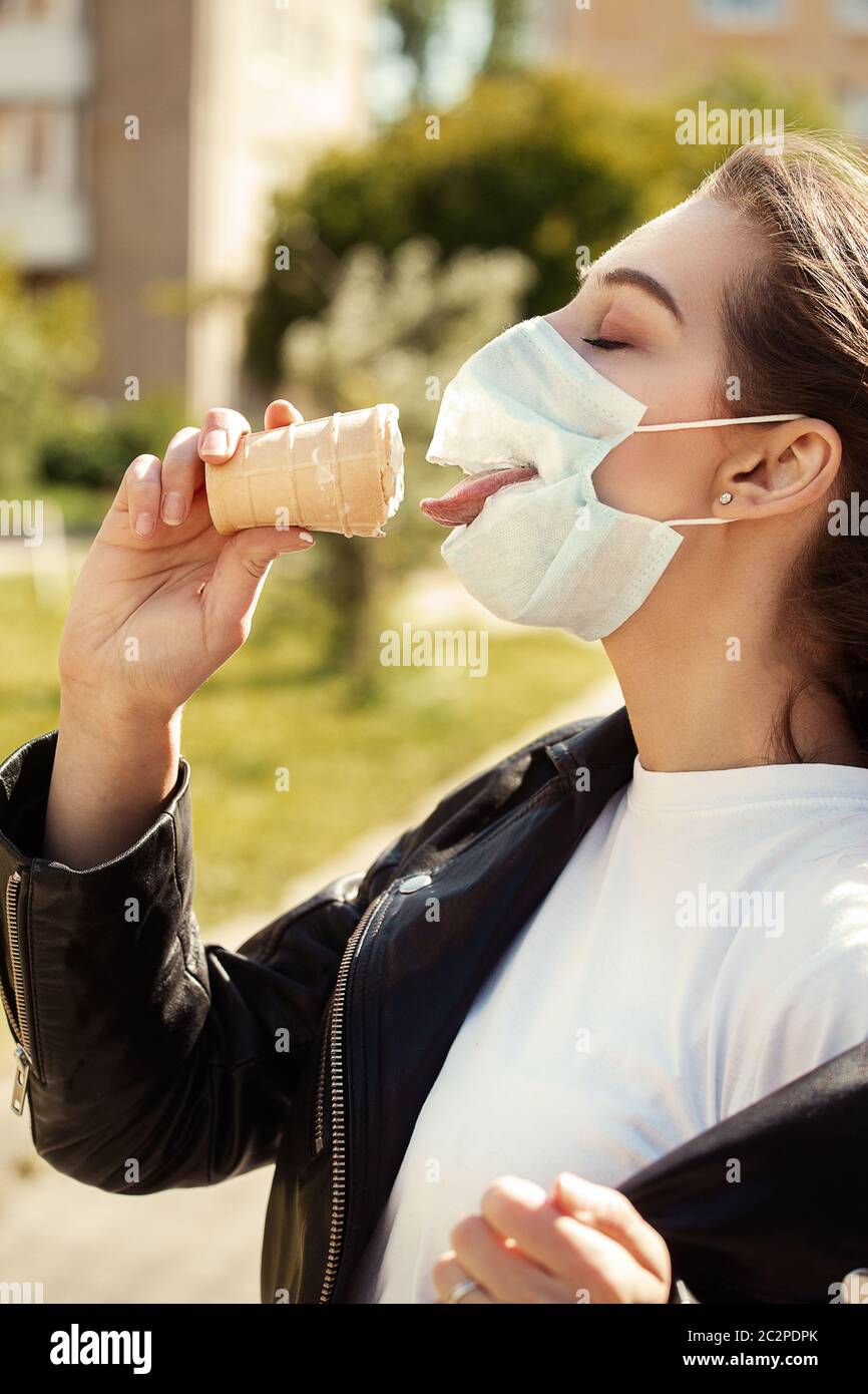 Fun junge Frau tragen medizinische Maske mit Loch und isst Eis Stockfoto