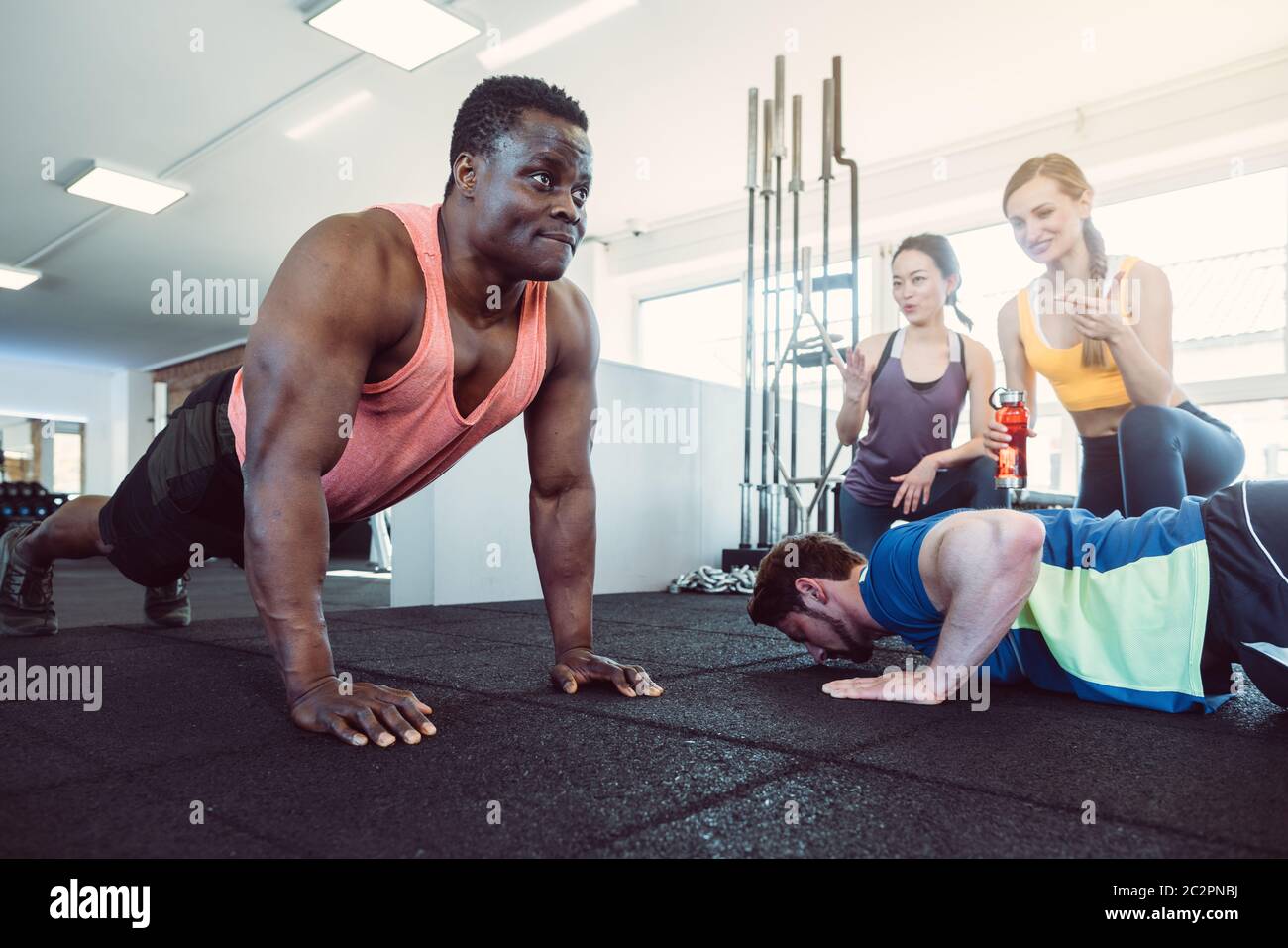 Zwei Männer haben einen Push-up-Wettbewerb im Fitnessstudio mit Mädchen jubeln sie Stockfoto