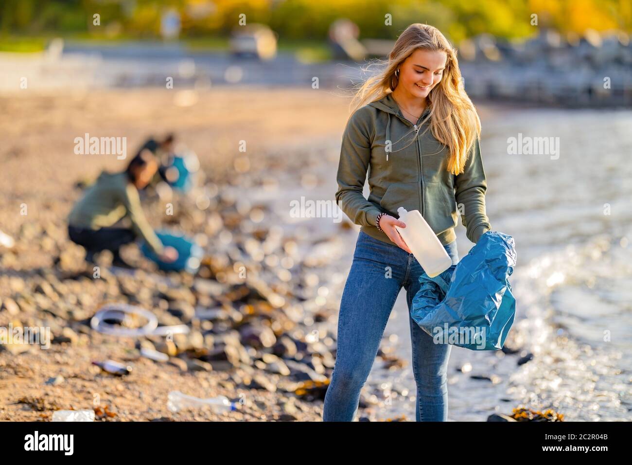 Lächelnd Junge weibliche Freiwillige hält Flasche und Müllbeutel am Strand Stockfoto
