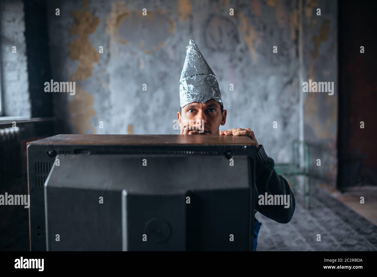 Angst Mann in Aluminiumfolie Kappe Fernsehen, Denkschutz, Paranoia Konzept. UFO, Verschwörungstheorie, Telepathie Phobie Stockfoto