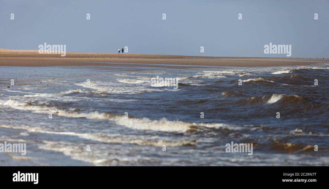 Zwei Personen, die in der Ferne am Strand von Thornham an der Nord-Norfolk-Küste, England, entlang gehen. Stockfoto
