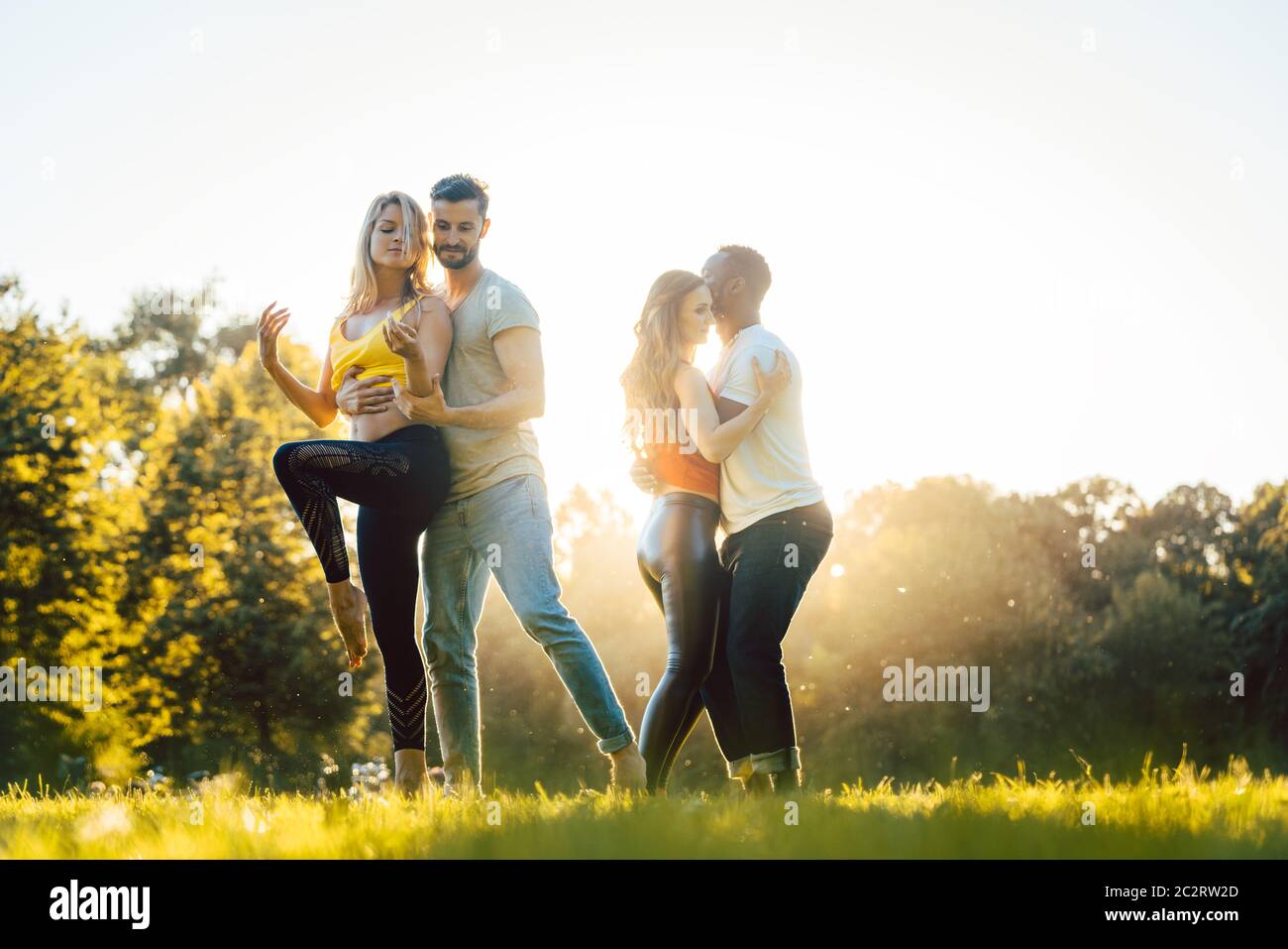 Zwei Paare machen während des Sonnenuntergangs in einem Park fortgeschrittene Tanzbewegungen Stockfoto