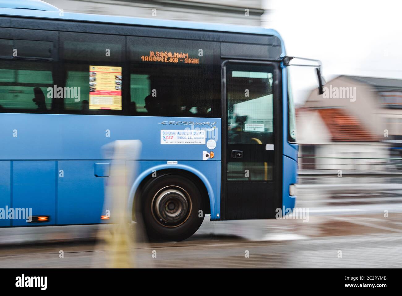 Blauer Bus fährt schnell auf der Regenstraße auf der Straße an launisch bewölktem bewölktem Tag Stockfoto