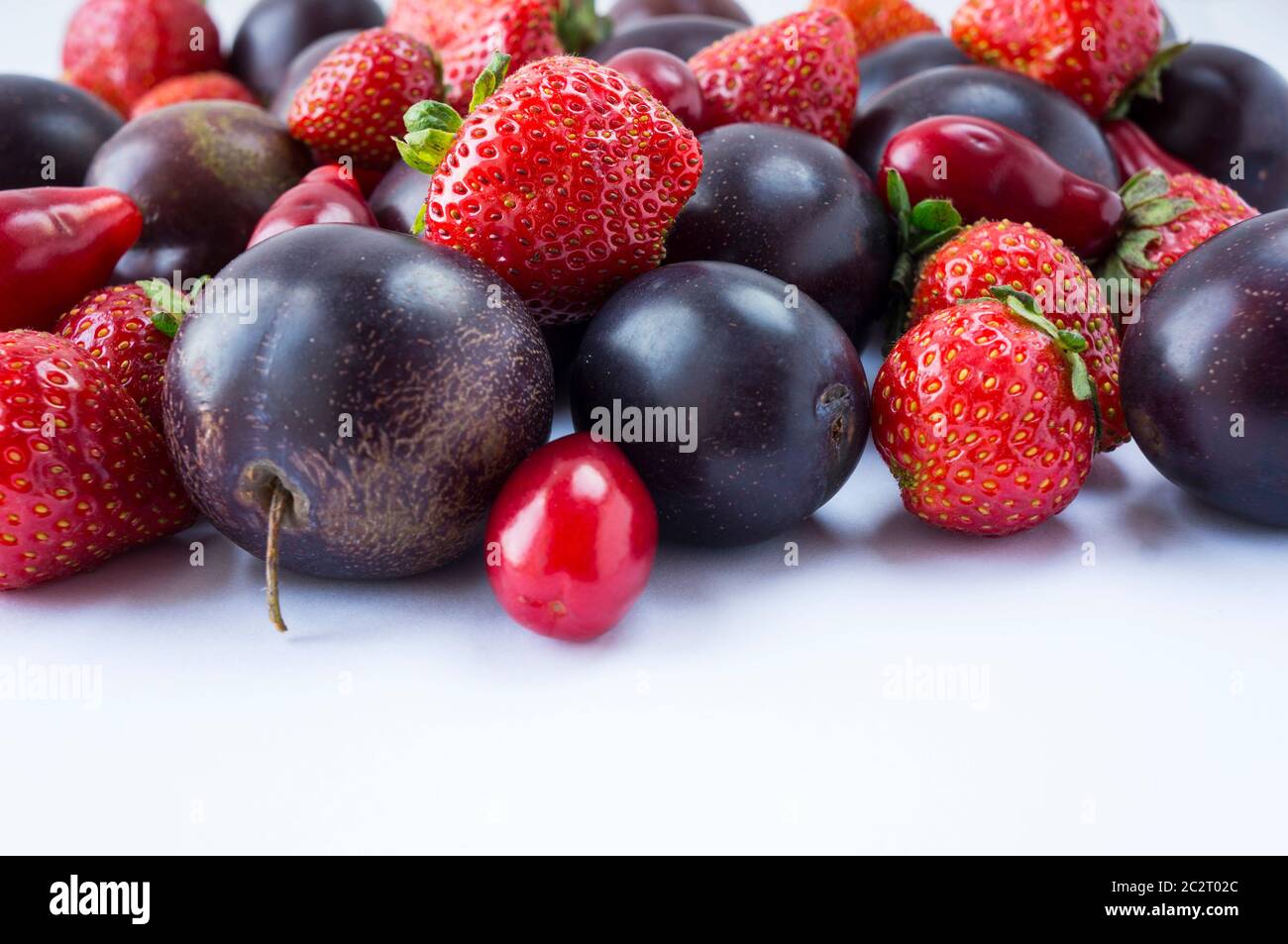 Verschiedene frische Sommerfrüchte. Reife Erdbeeren und Pflaumen auf weißem Hintergrund. Frische Früchte am Bildrand mit Kopierraum für Text. Hintergrund fru Stockfoto