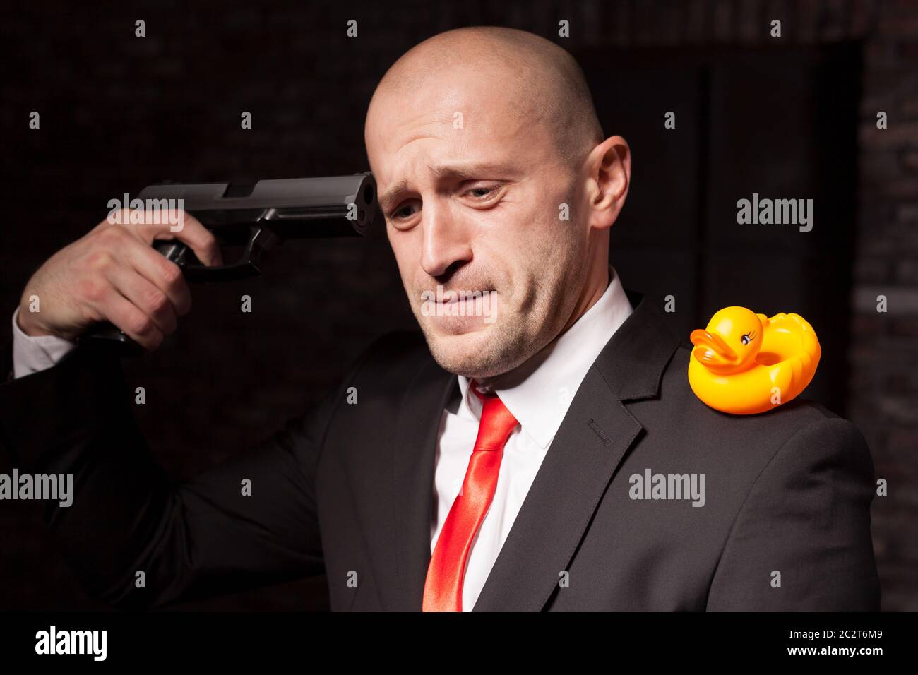 Vertrag Mörder in Anzug und roter Krawatte mit Spielzeug Ente auf Schulter zielt darauf ab, eine Pistole in den Kopf. Professionelle Geheimagenten Nervenzusammenbruch Konzept Stockfoto