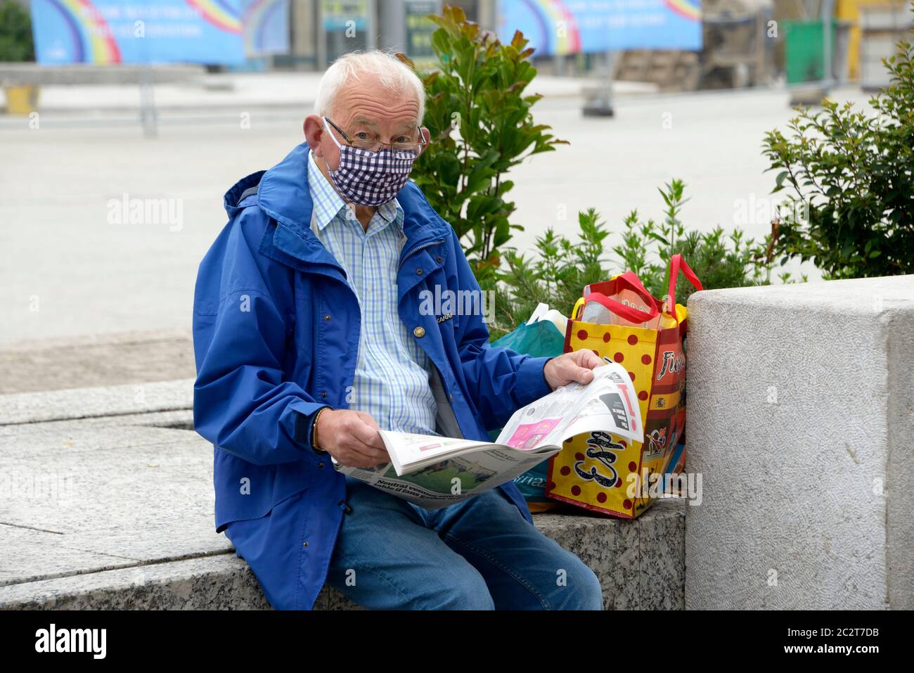 Mann mittleren Alters, Zeitung lesen, mit gepunkteten Maske, saß an einer Wand. Stockfoto