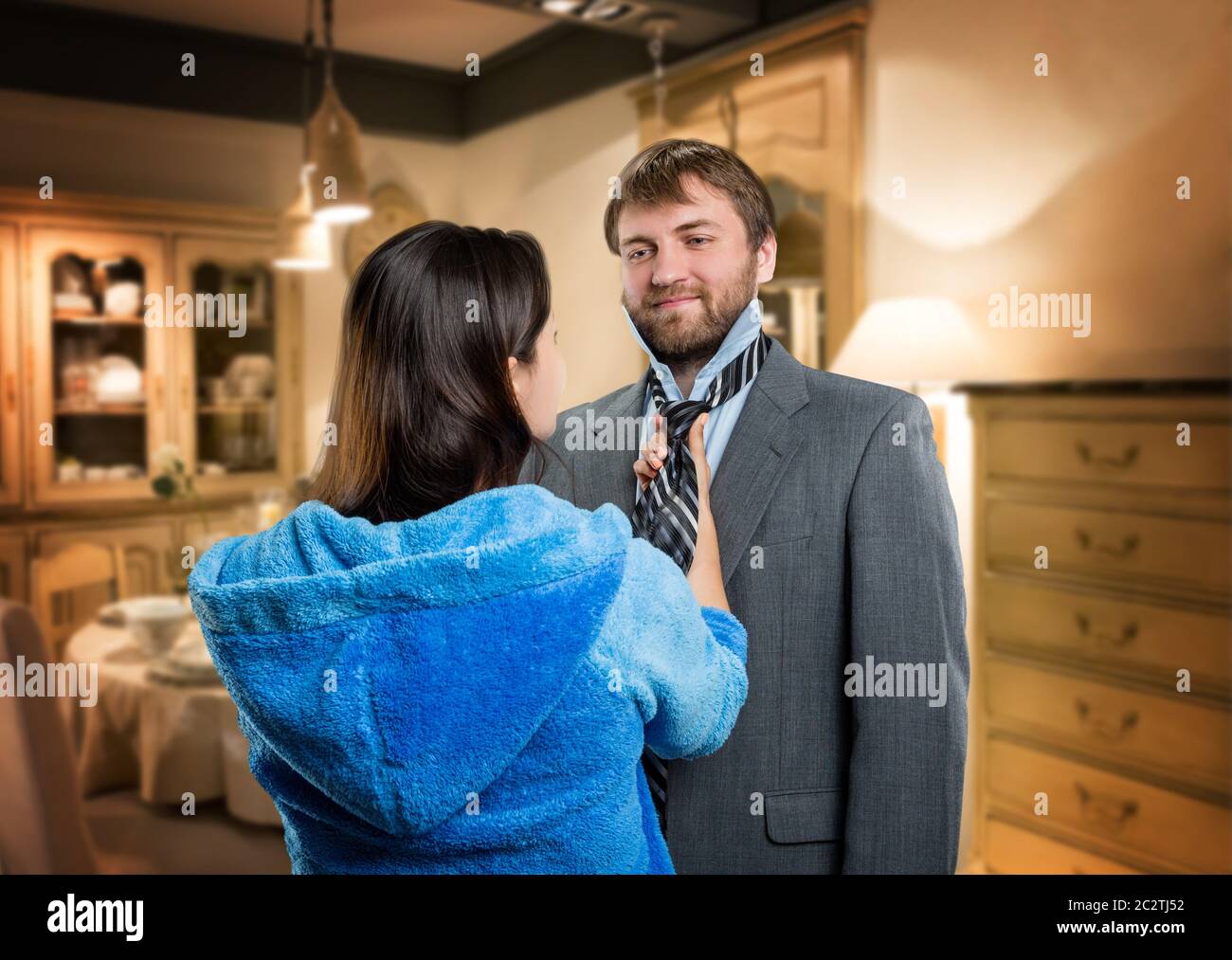 Junge Frau, die einen Krawatte zu ihrem lächelnden Mann aufgibt Stockfoto