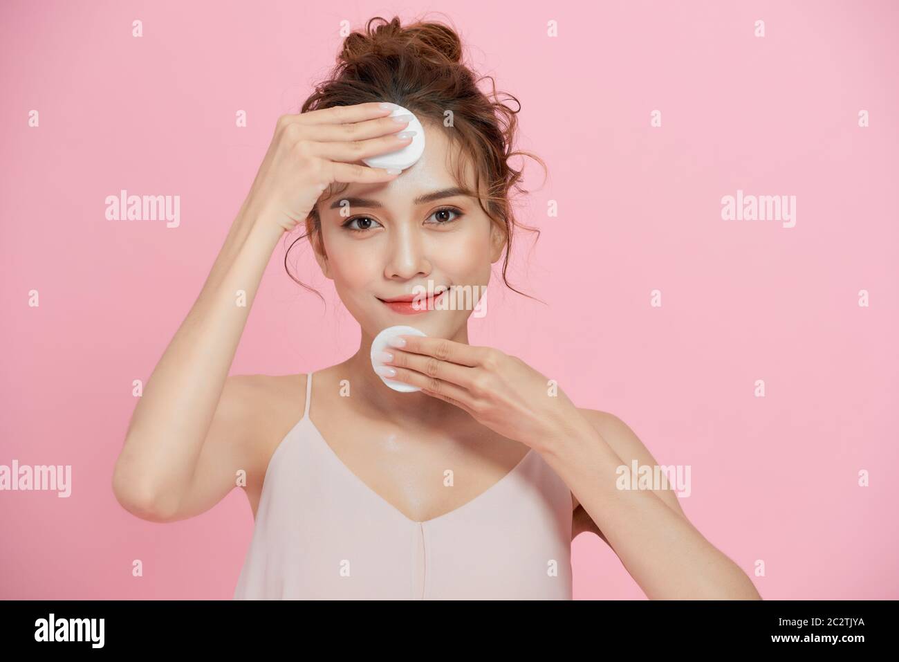 Nahaufnahme Schönheitsporträt einer lächelnden attraktiven Frau Reinigung ihr Gesicht mit einem Wattepad isoliert über rosa Hintergrund Stockfoto