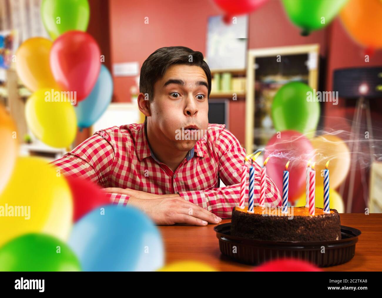 Geburtstagskind bläst Kerzen auf dem Kuchen in dekorierten Zimmer Stockfoto