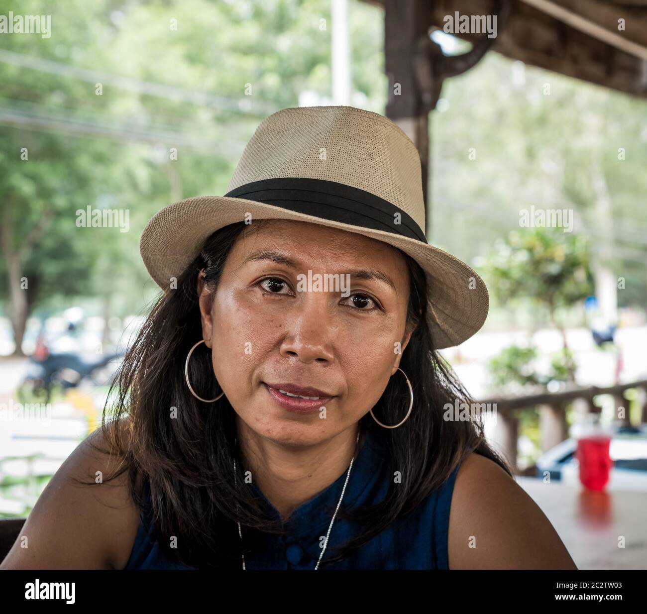 Frau im Café in weißen Fedora und trägt Reifen Ohrringe Blick auf die Kamera in Khao Lommuak Stockfoto
