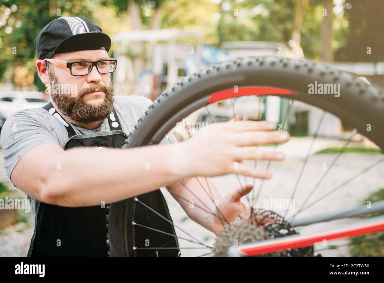 Fahrrad Handwerker arbeitet mit Fahrrad Rad, cycle Workshop Outdoor. Bärtige Mechaniker in Schürze Stockfoto