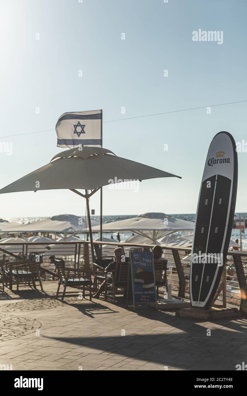 Tel Aviv / Israel-13/10/18: Touristen, die unter einem Sonnenschirm auf einem Strand am Mittelmeer in Tel Aviv ruhen; Longboard im Vordergrund, israelische n Stockfoto