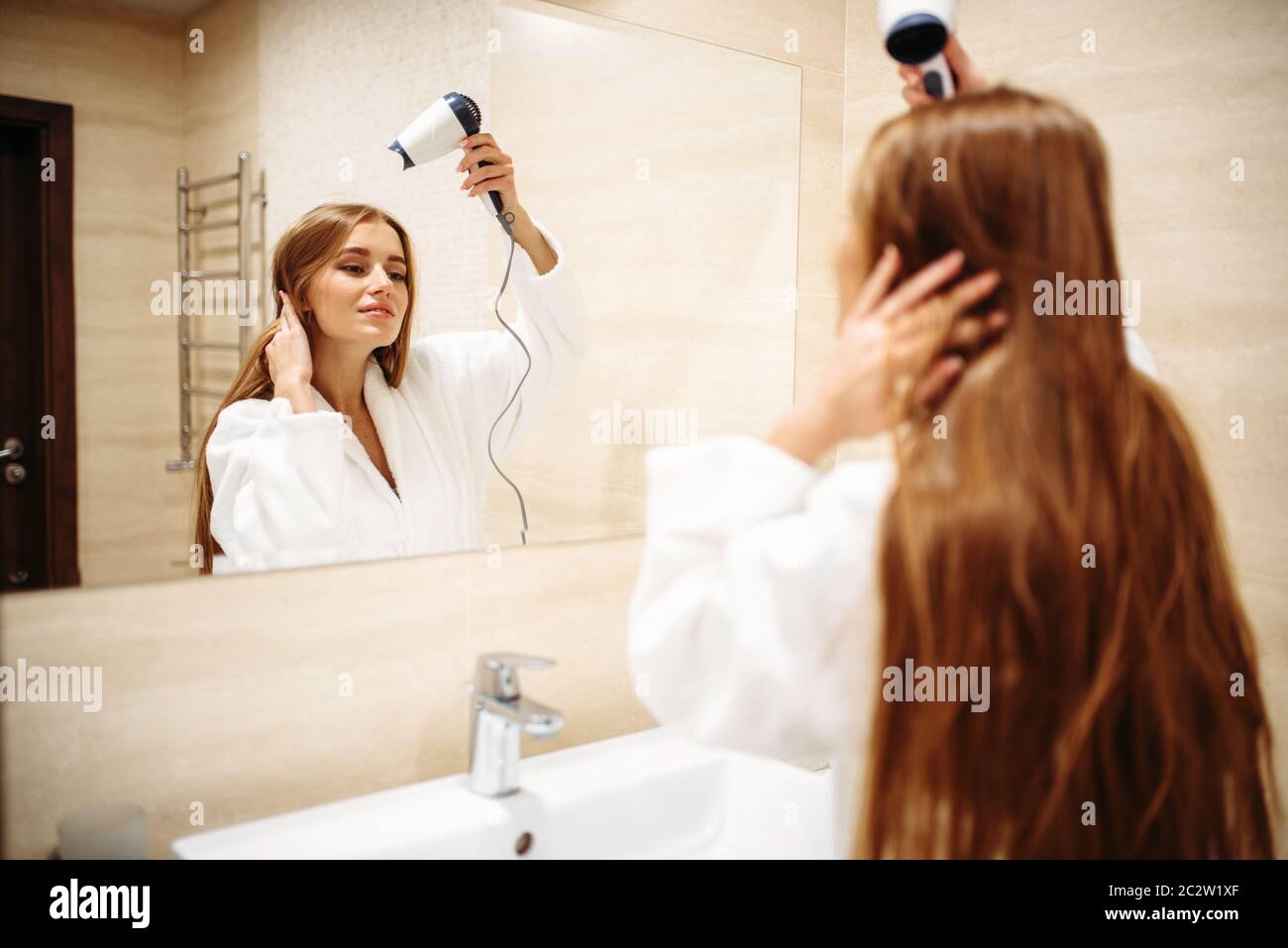 Schöne Frau im Bademantel Haare trocknen mit Trockner gegen Spiegel im Bad,  Hygiene, Schönheitspflege Stockfotografie - Alamy