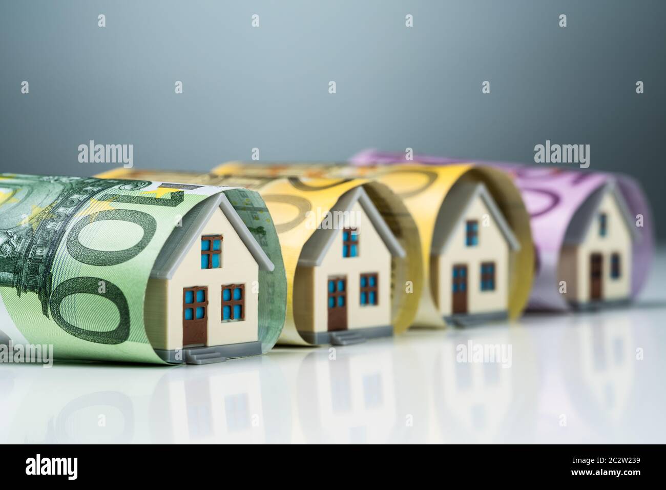 Reihe der Miniatur Häuser innerhalb der Euro-banknoten auf weißem Schreibtisch gegen grauer Hintergrund Stockfoto