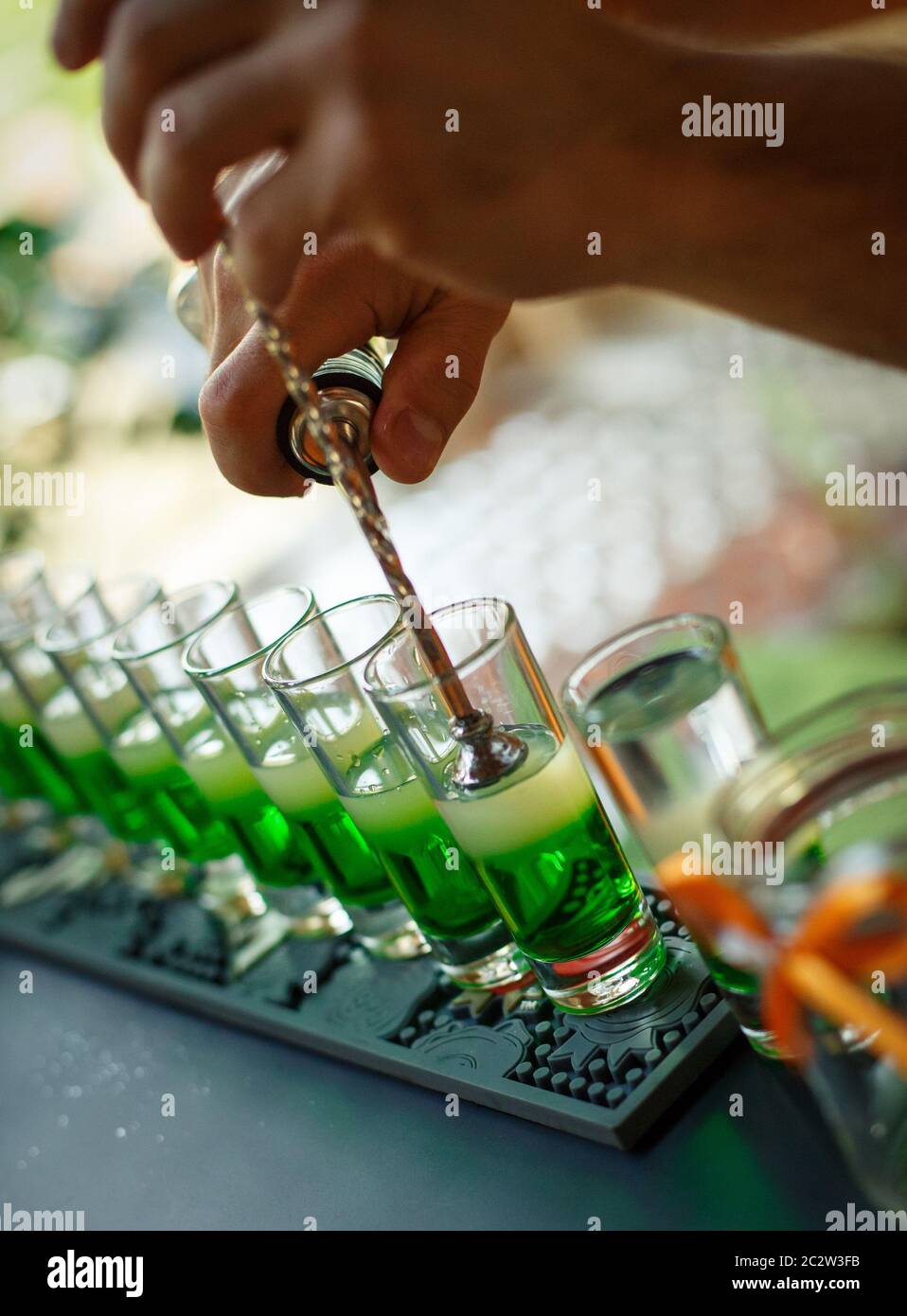 Barkeeper macht Alkoholschüsse an der Bar. Barkeeper bereitet grüne Cocktails für eine Party zu. Ein erfahrener Barkeeper mischt bunte Cocktails. Stockfoto