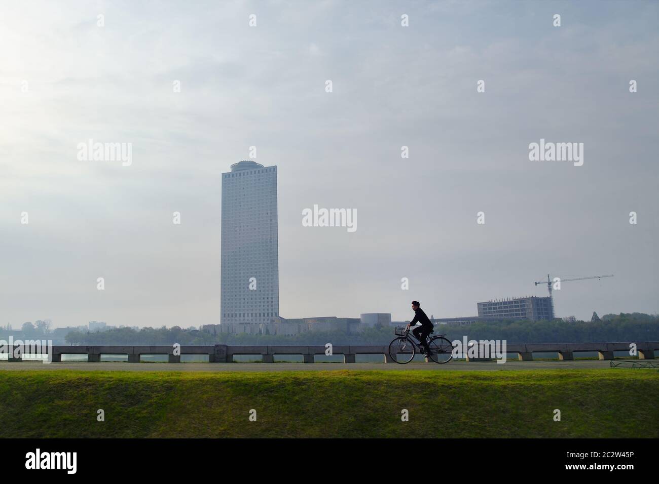 Pjöngjang, Nordkorea - 1. Mai 2019: Einheimischer, der bei Sonnenaufgang auf einem Fahrrad entlang des Taedong Flusses fährt. Modernes Yanggakdo Hotel im Hintergrund Stockfoto