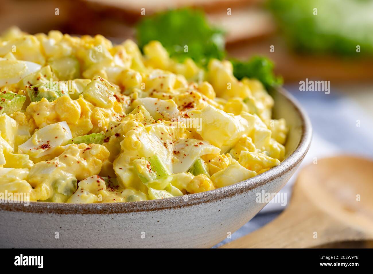 Nahaufnahme von Eiersalat in einer Schüssel mit Brotscheiben und Salat in Hintergrund aus dem Fokus Stockfoto