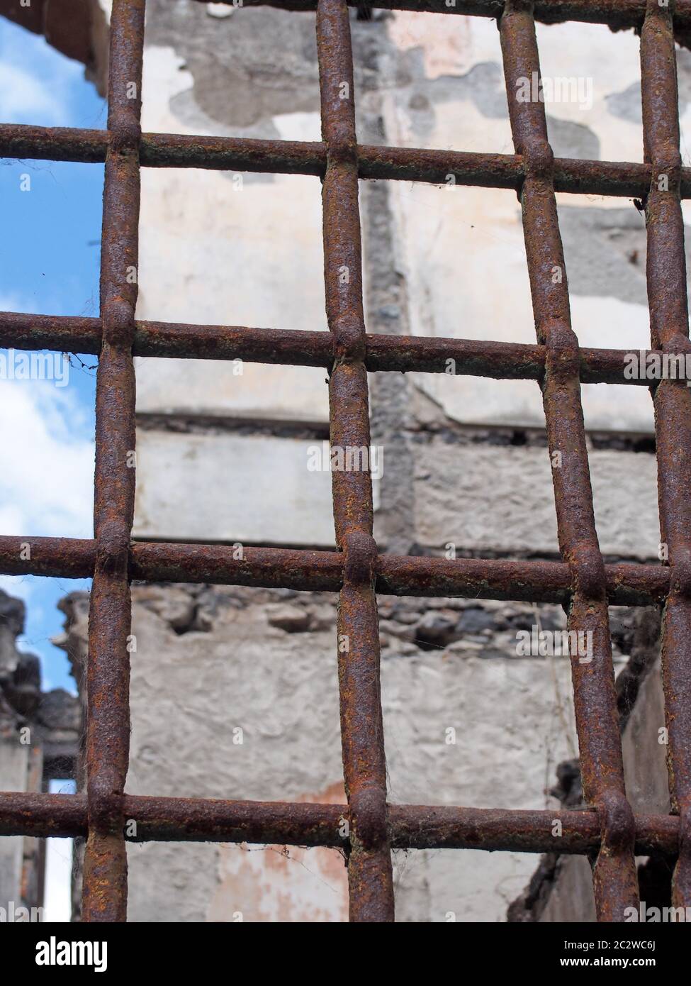 Nahaufnahme eines rostigen Eisenzauens mit Balken vor einem zerstörten einstürzenden Gebäude Stockfoto