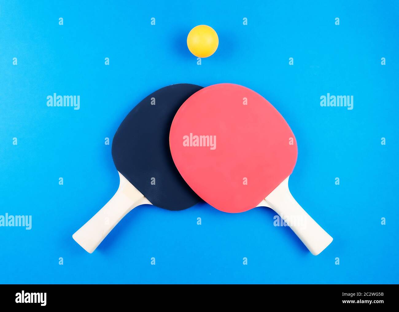 Direkt über Schuss von zwei Tischtennisschlägern und Ball auf blauem Hintergrund. Stockfoto