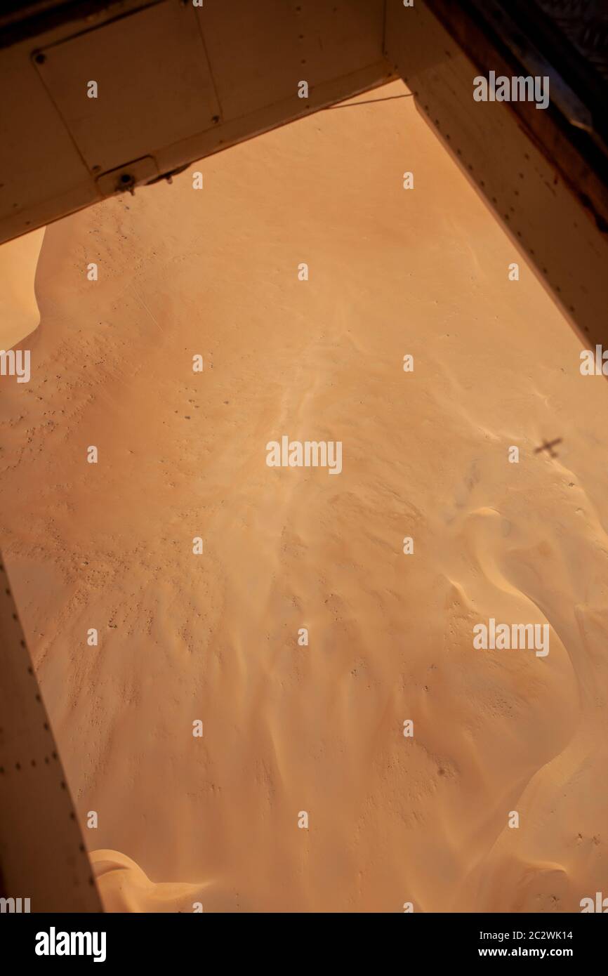Blick durch den offenen Boden einer Pilatues-Turboprop mit einer Triebwerke, die über Sanddünen in der Sahara, Nordafrika, fliegt. Stockfoto