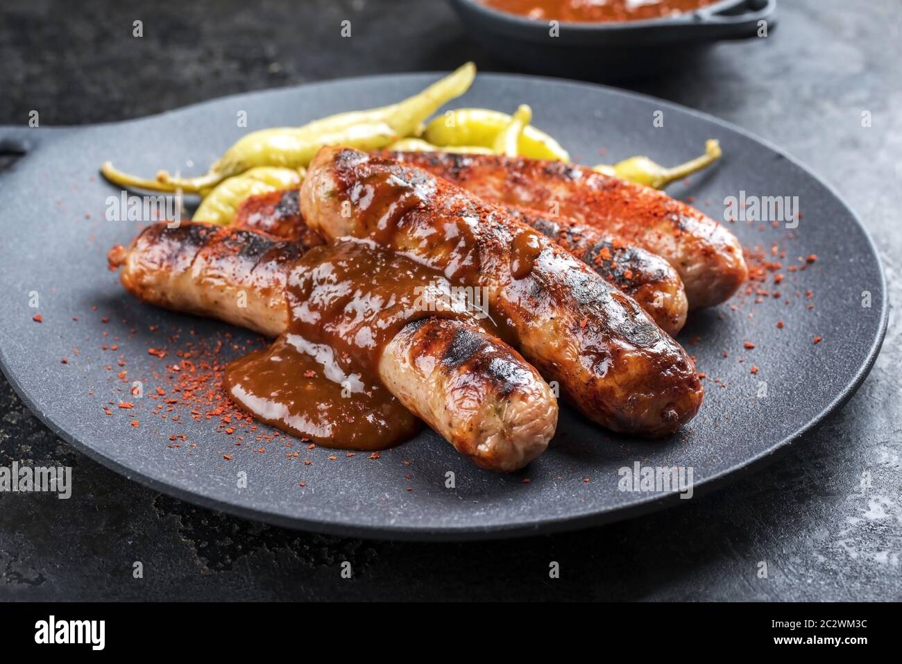Traditionelle deutsche Bratwurst mit heißer Sauce und Peperoni als Nahaufnahme auf einem modernen Design Gusseisen Teller Stockfoto